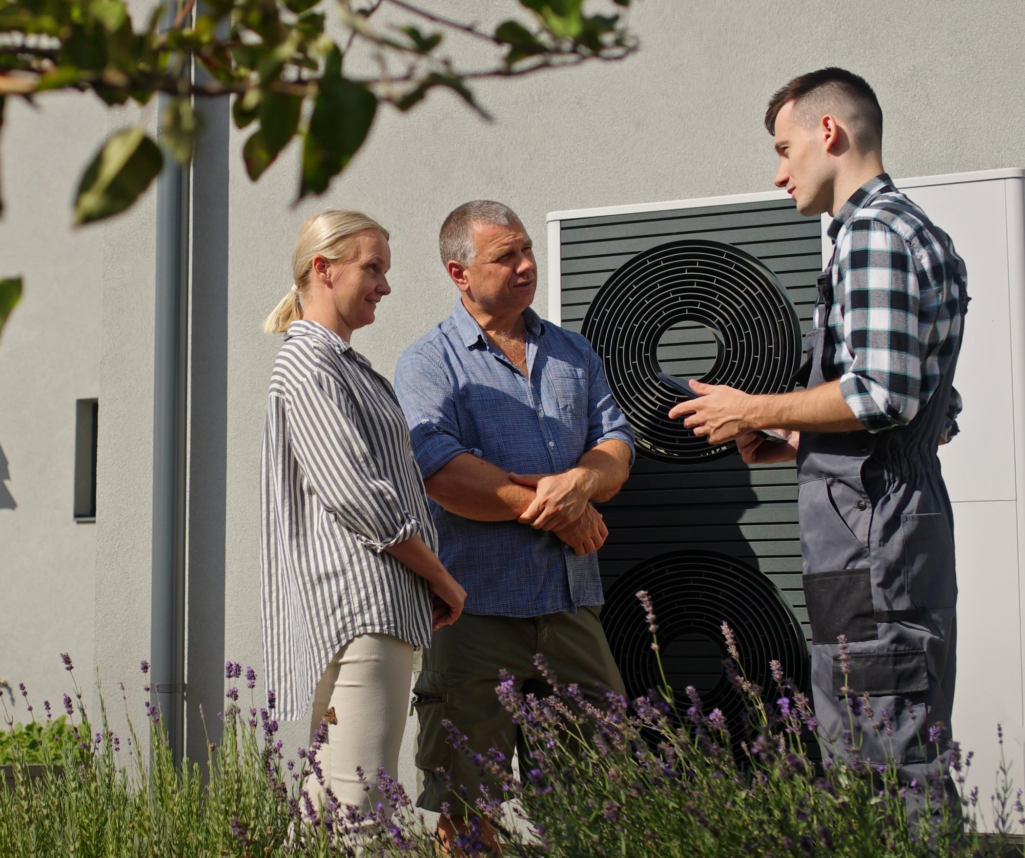 Technician explaining a heat pump to a homeowner couple outside their home